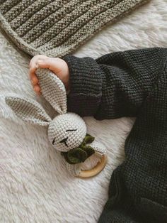 a small child is holding a crocheted bunny toy on a white rug with a black sweater