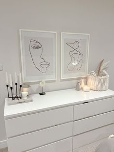 two framed art pieces on top of a white dresser next to candles and vases