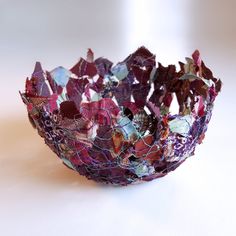 a bowl that is covered in purple and red paper flowers on a white table top