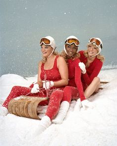 three women sitting in the snow with skis on