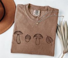 Autumn Pumkin T-shirt, Fall Trendy Shirt, Fall sweatshirt, Pencil Drawing Fall Mushroom, Pumpkin Tee, Boho rustic shirt, Retro Fall Shirt HOW TO ORDER 1. Choose the color of the clothing 2. You can choose the Clothing & size  (Please check the size chart product images for more details) 3. Please tell me if you have personalization (Optional) 4. DONE PRODUCTION &SHIPPING TIME Production time and shipping time can vary depending on the number of order we have in progress. Estimated production tim Brown Screen Print Top For Fall, Relaxed Fit Fall Tops With Mushroom Print, Relaxed Fit Top With Mushroom Print For Fall, Relaxed Fit Mushroom Print Top For Fall, Fall Mushroom Design Crew Neck T-shirt, Fall Crew Neck T-shirt With Mushroom Design, Cotton T-shirt With Mushroom Design For Fall, Fall Mushroom Print Graphic T-shirt, Fall Mushroom Print Graphic Tee