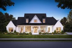 a white house with black roof and windows on the front lawn at night in an upscale neighborhood