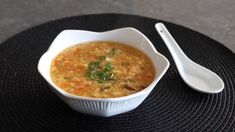 a white bowl filled with soup on top of a black place mat next to a spoon