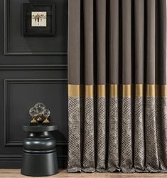 a black and brown curtain with gold trim in a room next to a small table