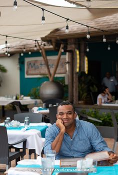 a man sitting at a table in front of an open air dining area with tables and chairs