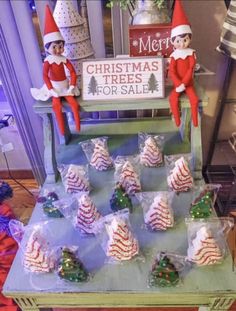 two elfs sitting on top of a table with christmas trees for sale