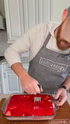 a man in an apron is decorating a cake with red icing on it