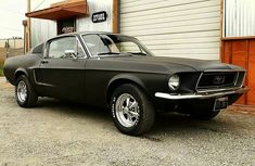 an old black mustang parked in front of a building