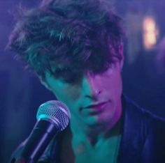 a man with curly hair holding a microphone in front of a purple and blue background