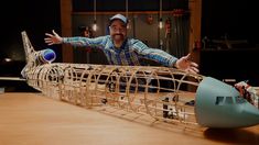 a man standing in front of a model boat on top of a wooden table next to a blue ball