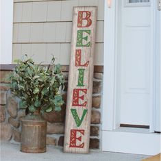 a wooden sign that says believe next to a potted plant on the front porch