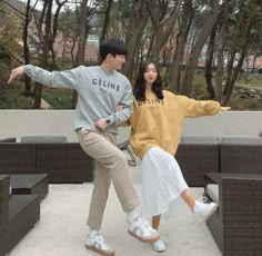 a man and woman dancing in front of some trees with their arms out to each other