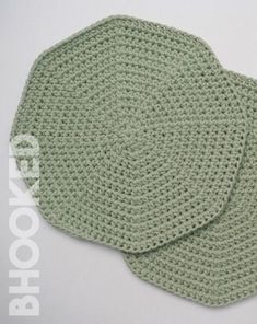 two green crocheted coasters sitting next to each other on a white surface