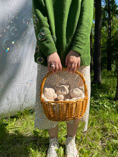 a woman holding a basket full of teddy bears in the grass with bubbles behind her