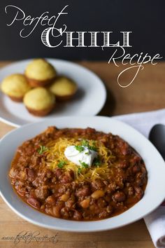 a bowl of chili with cheese on top next to some mini muffins and a napkin