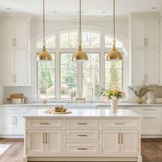 a large kitchen with white cabinets and gold pendant lights hanging from the ceiling over the island