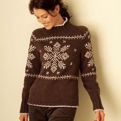 a woman wearing a brown sweater with white snowflakes on it, leaning against a wall