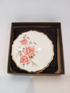 a white plate with pink flowers on it in a black and gold box against a white background