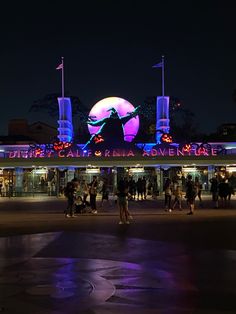 people are walking around in front of a building with lights and decorations on it at night