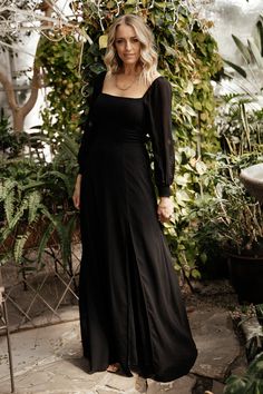 a woman wearing a black dress standing in front of plants