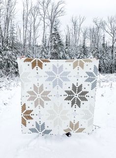 a white quilt with brown and gray designs on it in the middle of snow covered ground