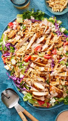 a large salad with chicken, lettuce and tomatoes on it next to some dipping sauces