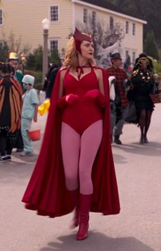 a woman in a red costume is walking down the street with other people behind her