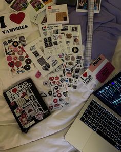 an open laptop computer sitting on top of a bed next to various stickers and magnets