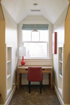 a red chair sitting in front of a window next to a desk with a lamp on it