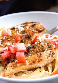 a white bowl filled with pasta and chicken topped with tomatoes, parmesan cheese and herbs