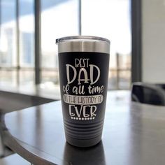 a black and silver cup sitting on top of a table next to a large window