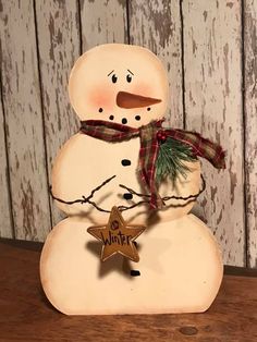 a wooden snowman with a red and green scarf on it's head, holding a star ornament