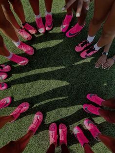 a group of people standing in a circle with pink shoes on top of green grass