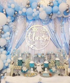 a table topped with lots of blue and white balloons next to a wall covered in snowflakes