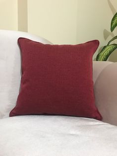 a red pillow sitting on top of a white couch next to a potted plant