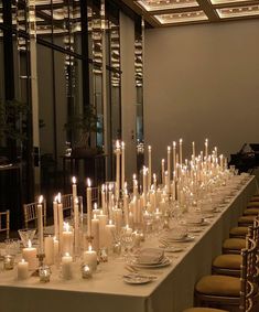 a long table with many lit candles on it and plates in front of the tables