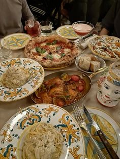 a table full of plates and bowls with food on them including pizza, pasta, bread