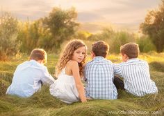 three people sitting in the grass with their backs to each other and looking at something