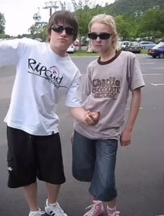 two young people standing next to each other in a parking lot with their arms outstretched