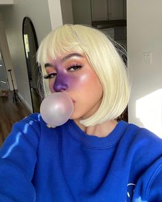 a woman with blonde hair and blue sweater blowing bubble