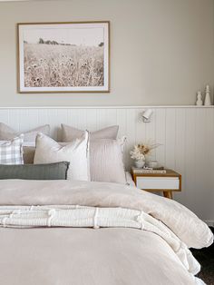 a bed with white linens and pillows in a small room next to a painting on the wall