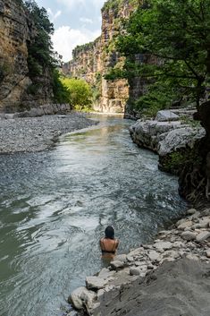 a man standing in the middle of a river surrounded by rocks and trees on both sides