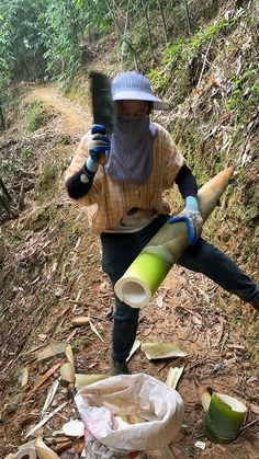 a person in a hat and mask holding a large object on the side of a dirt road