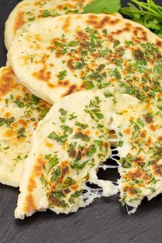 cheese stuffed naan bread is cut in half and placed on a black plate with green garnish