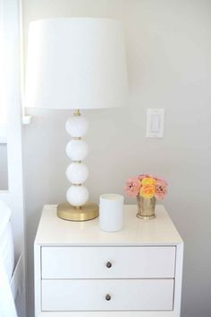 a white nightstand with flowers and a lamp on top