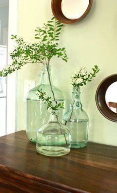 two vases with flowers are sitting on a dresser in front of a wall mirror