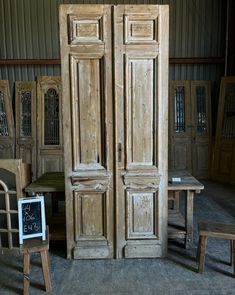 an old wooden armoire next to two chairs and a table with a chalkboard on it