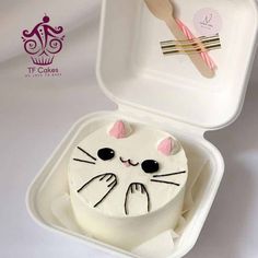 a white cake in a plastic container with a cat face painted on the side and fork sticking out of it