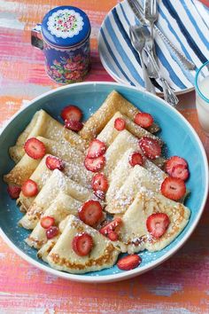 pancakes with strawberries and powdered sugar in a blue bowl next to a glass of milk