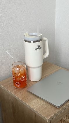 a laptop computer sitting on top of a wooden table next to a cup and drink